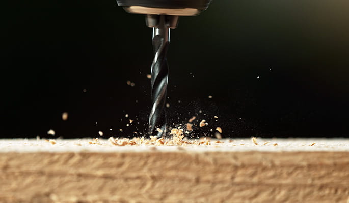 A close up of a screw being drilled into a plank of wood.