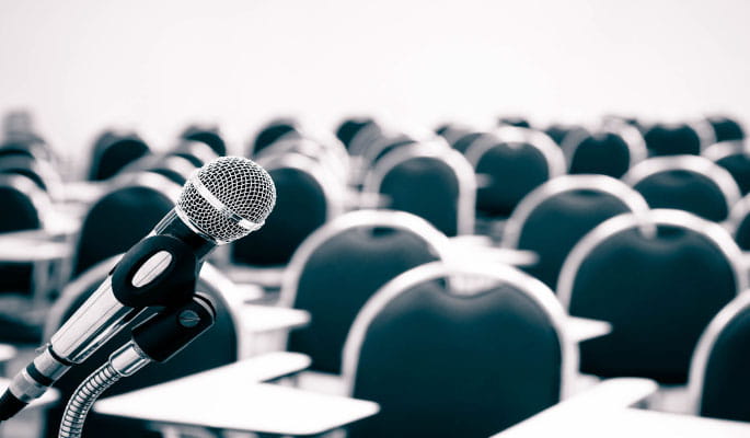 Image of a microphone in front of delegate chairs at an event 
