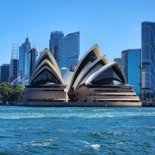 Royal Sydney Opera House by water with cityscape in background